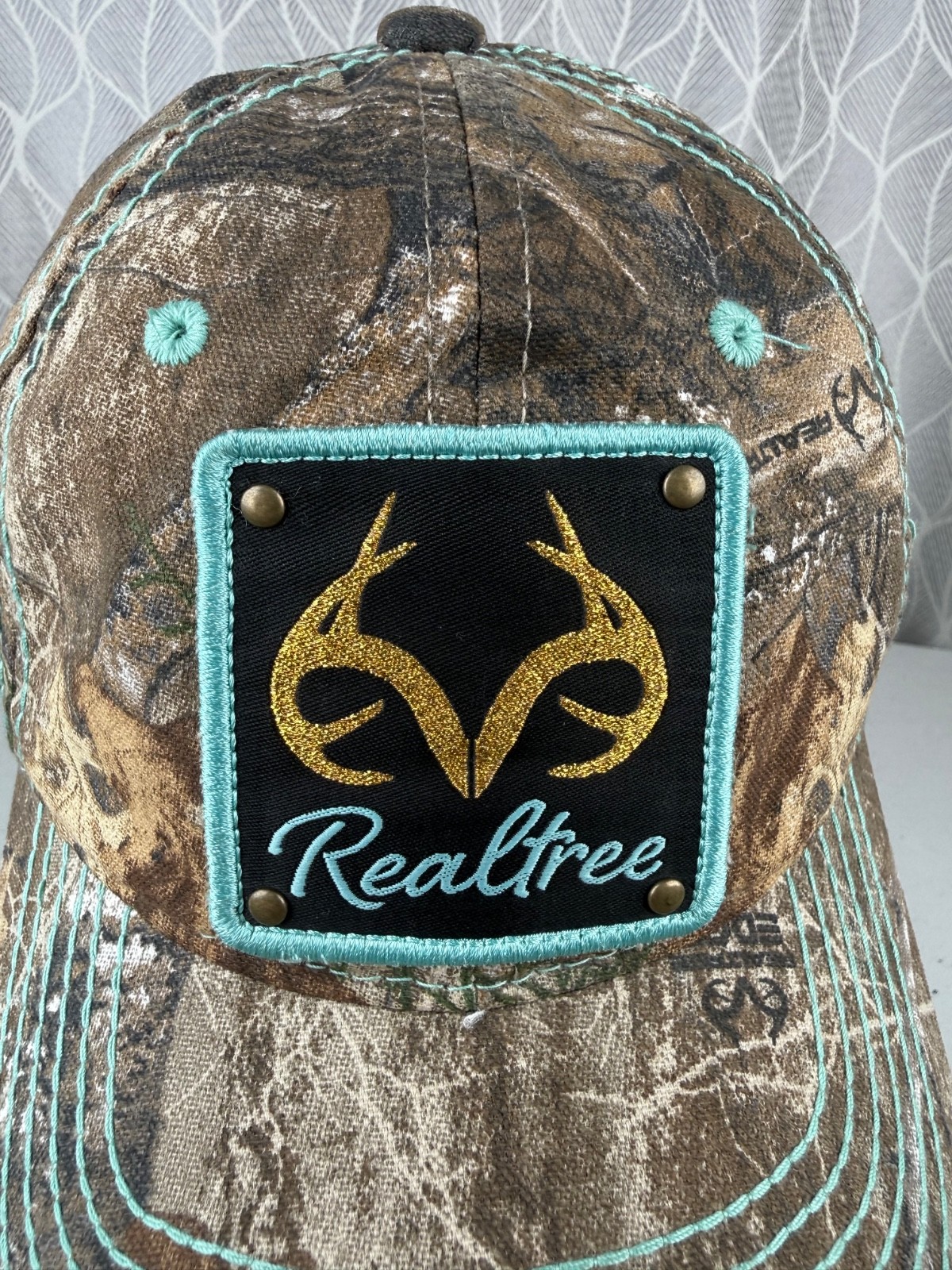 Real Tree Gold Sparkle Logo Black Aqua Rivet Patch on Camouflage Hat Cap