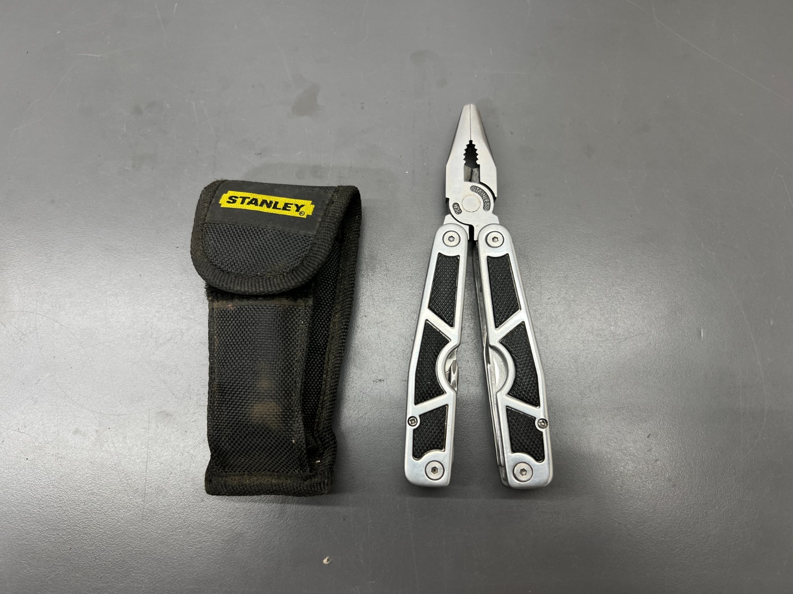 (q) UNUSED STANLEY 2CR 12 IN 1 STAINLESS KNIFE PLIER DRIVER W CASE & BITS