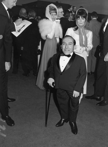 Michael Dunn smiles stands a cane while posing in front of a crowd- Old Photo
