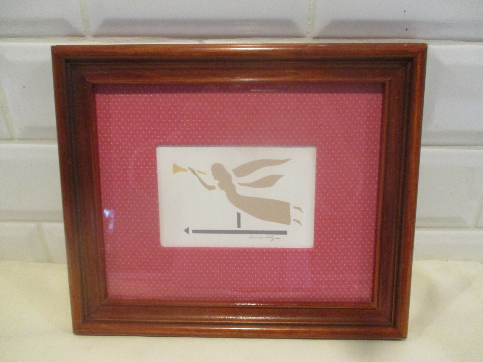 Framed flying angel with horn, signed and under glass.